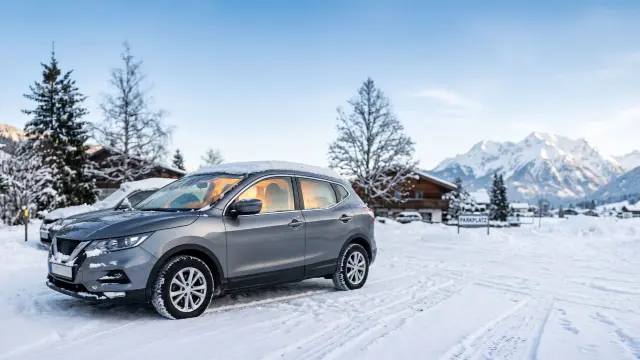 Auto auf einem Parkplatz im Winter umgeben von Schnee, Tannen und Bergen